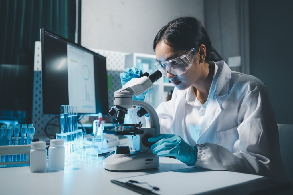 Young scientists in sterile clothing and safety goggles sitting at table conducting research investi