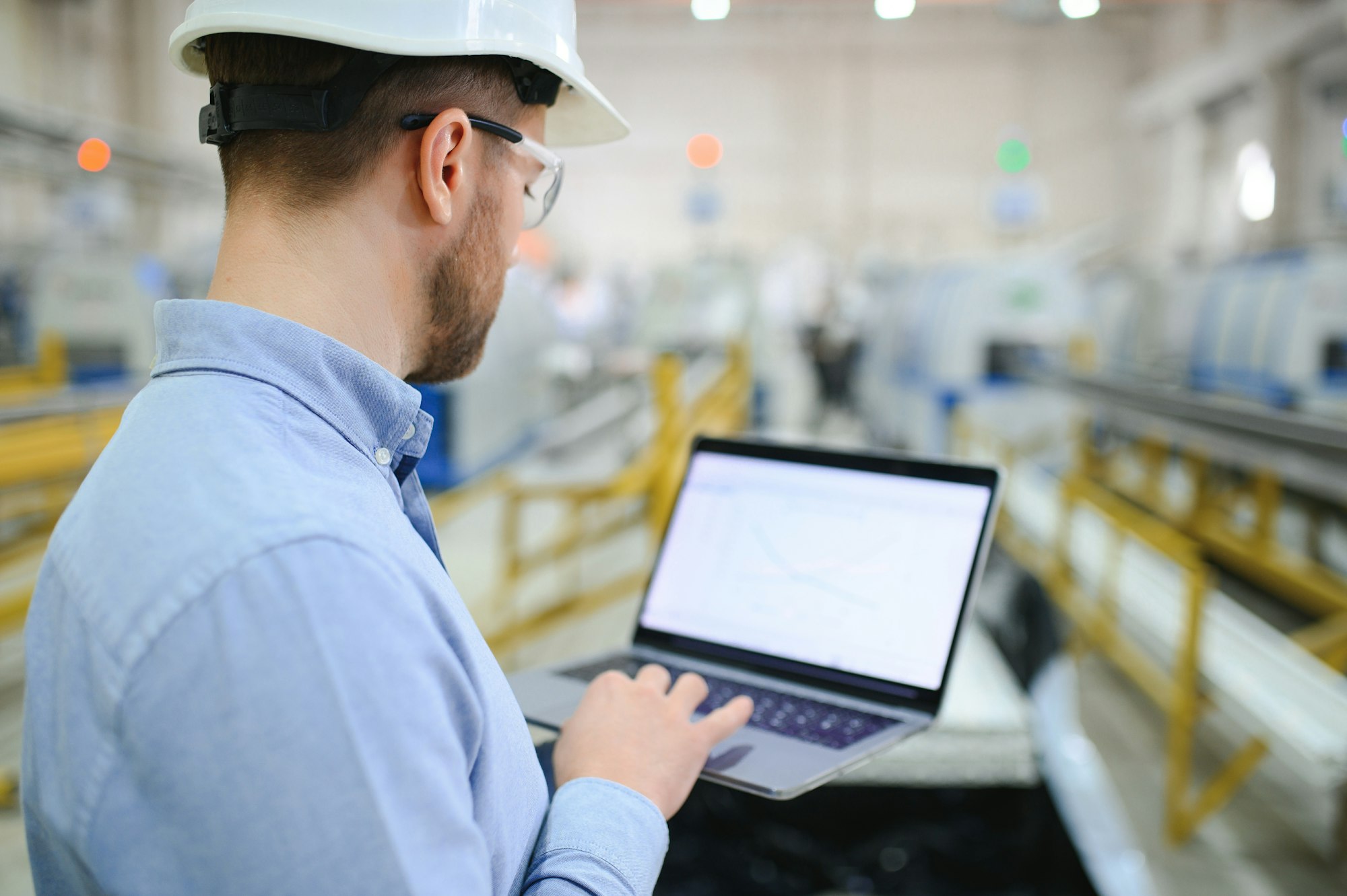 Side view of technician or engineer with headset and laptop standing in industrial factory